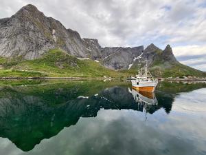 a boat in a body of water with mountains at Lofoten Bed & Breakfast Reine - Rooms & Apartments in Reine