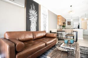 a living room with a brown leather couch and a kitchen at Avemore Jan Cats No 3 in Stellenbosch