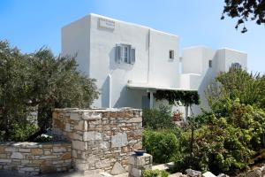 a white house with a stone wall and trees at Flora & Agelos Studios - Paros in Chrissi Akti