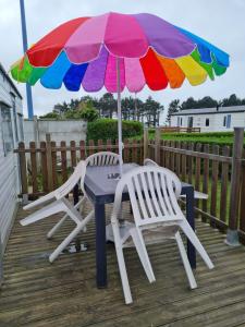 two chairs and a table with an umbrella on a deck at Mobilhome empl 28 in Saint-Martin-aux-Buneaux