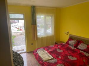 a bedroom with a bed with a red comforter and a window at Семеен Хотел Сандим in Kŭrdzhali