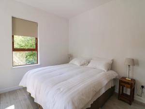 a white bedroom with a large bed and a window at The Mews Suskar in Glendarragh