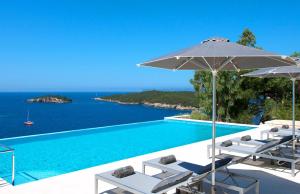 a pool with chairs and an umbrella and the ocean at White Orchid in Syvota