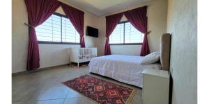a bedroom with two windows and a bed with a rug at L'Oasis in Mzerguia