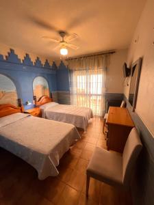 a bedroom with two beds and a table and a desk at Pensión El Alamo in Lepe