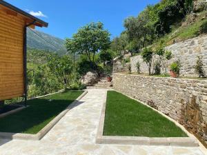 a garden with a stone wall and green grass at Guesthouse Deshnica in Këlcyrë