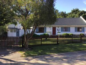 a white house with a fence and a tree at Knysna Holiday Cottage in Knysna