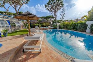 a swimming pool with lounge chairs and an umbrella and a swimming pool at Villa CHELSEA in Vilamoura