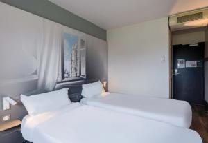 two beds in a small room with white sheets at B&B HOTEL Beauvais in Beauvais