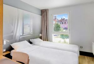 two beds in a room with a window at B&B HOTEL Dunkerque Centre Gare in Dunkerque