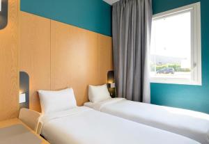 two beds in a room with a window at B&B HOTEL Lieusaint Carré Sénart in Lieusaint