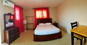 a bedroom with a bed and a desk and red curtains at Complexe La Belle Rosie in Les Cayes