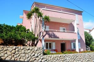 una casa rosa con palmeras frente a una pared de piedra en Apartments Ena, en Vrboska