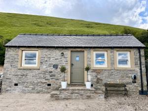 a stone cottage with a green hill in the background at Luxury cottage for 2 in Castleton - Peak District retreat - Panoramic Views & Log burner in Castleton