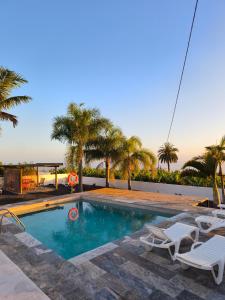 a swimming pool with two lawn chairs and palm trees at Los Padres B in Puerto de Tazacorte