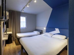 a hotel room with two beds and a blue wall at ibis Budget Millau Viaduc in Millau