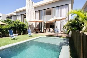 a swimming pool in front of a house with umbrellas at Oka Milagres Beachfront Condominium By MME in Barra do Camaragibe