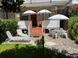 a patio with white chairs and tables and umbrellas at il giardino del mirto in Vicarello