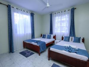 two beds in a room with blue curtains and windows at Serene Coastal Suites in Mombasa
