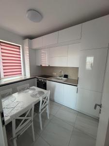 a white kitchen with a table and a sink at C&A Apartment in Giroc