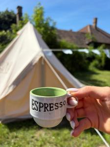 a person holding a coffee cup in front of a tent at The Ozorian Rooms & Glamping in Ozora