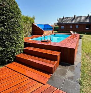 a swimming pool with a wooden deck next to a house at Zefir Domek nr 5 in Dąbki