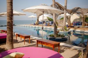 a pool with benches and umbrellas next to the ocean at The Xperience by g & Beach Club in Mazatlán