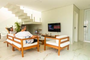 two men sitting in a living room watching tv at Casa Estrela do Mar in Maragogi