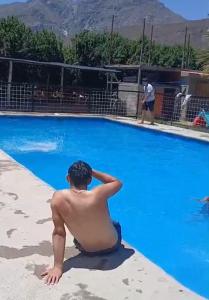 a man sitting on the side of a swimming pool at Agro Camping Los Costeños in Choapa