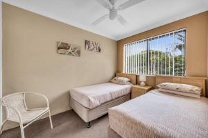 a bedroom with two beds and a chair and a window at Hydra 8 in Merimbula +4 photos
