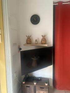 a clock on a wall above a television on a shelf at Maison avec piscine proche plage in Les Trois-Îlets