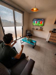 a man sitting on a couch watching tv in a living room at Luminoso departamento cerca de bodas y jardines! in Atlixco