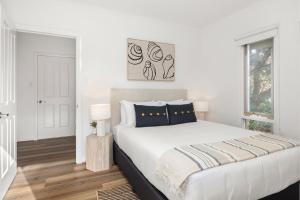 a white bedroom with a large bed and a window at Sunset Drift Edithvale Steps to Beach in Edithvale