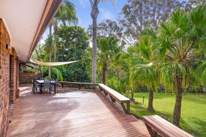 a deck with a table and chairs and palm trees at Kookaburra Retreat in Berkeley Vale