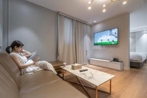 a woman sitting on a couch watching tv in a living room at Bergen Hotel Daejeon Yuseong in Daejeon
