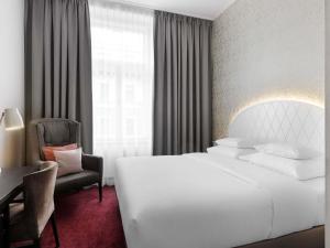 a hotel room with a large white bed and a chair at Hotel Rathauspark Wien - Handwritten Collection in Vienna