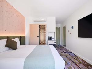 a bedroom with a large bed and a flat screen tv at Novotel St Kilda in Melbourne