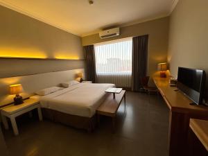 a bedroom with a bed and a television and a desk at Bali World Hotel in Bandung