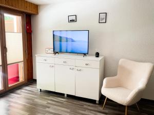 a white dresser with a television and a chair at Nendaz Alpine Studio - Ski & Swimming Pool in Nendaz
