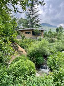 a house on a hill next to a stream at Sarayu Farmstays in Manāli +12 photos