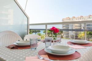 a table with plates and glasses and a vase with a pink flower at Maria apartment in Blanes