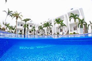 a large swimming pool in front of a building with palm trees at El Cielo Resort in Dauin