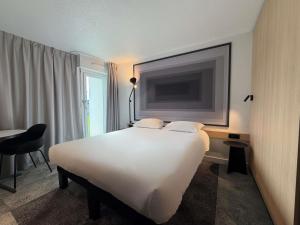 a hotel room with a white bed and a flat screen tv at ibis Rennes Beaulieu in Cesson-Sévigné +101 photos