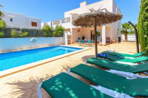a villa with a swimming pool with green chairs and an umbrella at Villa Lagoa in Cala Dor in Cacla D'or