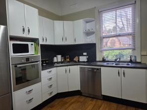 a kitchen with white cabinets and a sink and a microwave at The Red Manor on Mort in Lithgow