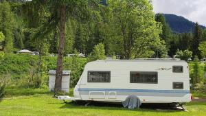 a white caravan parked in a field next to a tree at Brigga Camping Mietwohnwagen in Ritzingen