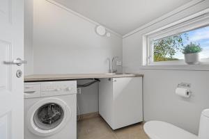 a white laundry room with a washing machine and a window at Beach cottage in Søgne in Kristiansand