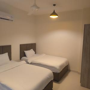 two beds in a room with white sheets and a light at Golden Seasons Rose in Salalah