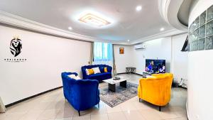 a living room with blue and yellow chairs and a tv at Residence Le Carat in Douala