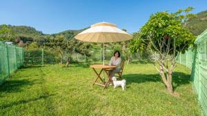 a woman sitting at a table under an umbrella with a dog at Yeosu Everyday Small Changes Pension in Yeosu